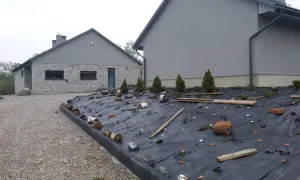 Jak położyć agrowłókninę na skarpie: czarna agrowłóknina zabezpiecza skarpę przed erozją, z widocznymi pachołkami, drewnem i roślinami.