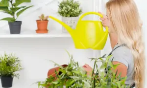 Dziewczyna z długimi blond włosami podlewa rośliny żółtą konewką. Dbanie o kwiaty to ważna czynność, a pytanie "jak często podlewać kwiaty" jest kluczowe dla ich zdrowia.