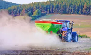 Traktor rozsiewa wapno, pomagając odkwasić glebę. W tle las i pole.