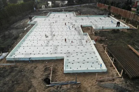 Fundament punktowy z rur szalunkowych, przygotowany do wylania betonu. Na placu budowy widać zbrojenie i izolację.