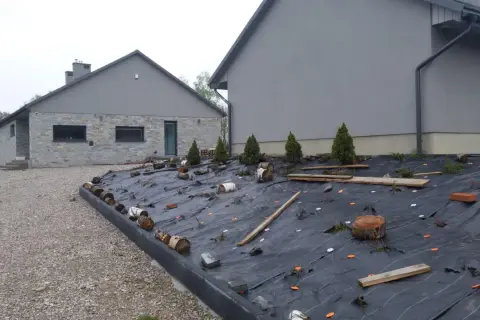 Jak położyć agrowłókninę na skarpie: czarna agrowłóknina zabezpiecza skarpę przed erozją, z widocznymi pachołkami, drewnem i roślinami.