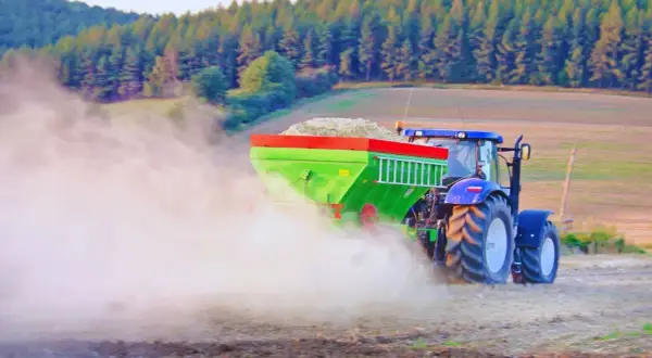 Traktor rozsiewa wapno, pomagając odkwasić glebę. W tle las i pole.
