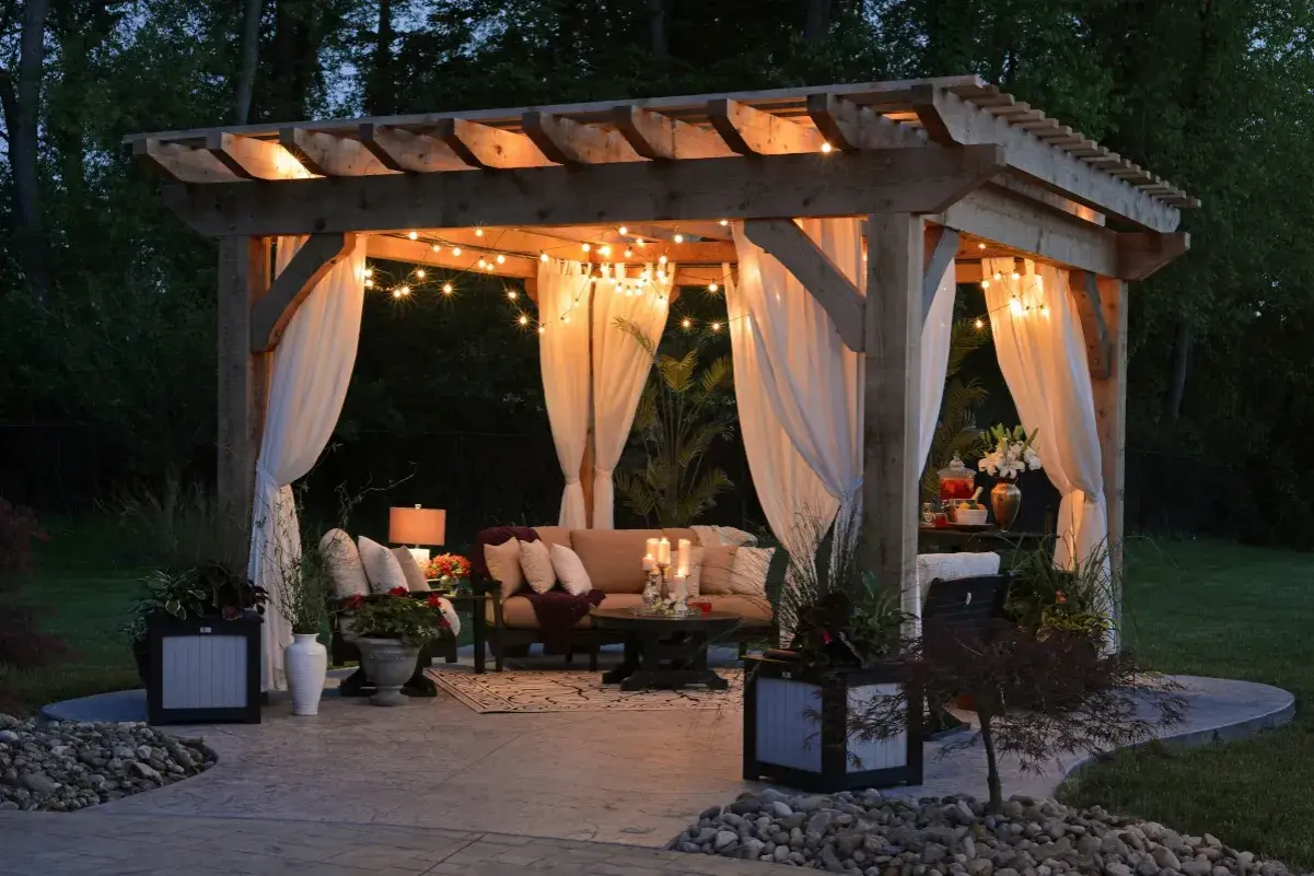 Urocza pergola z oświetleniem i zasłonami, idealna na letnie wieczory. Inspiracja, jak zrobić pergole, by stworzyć przytulne miejsce.
