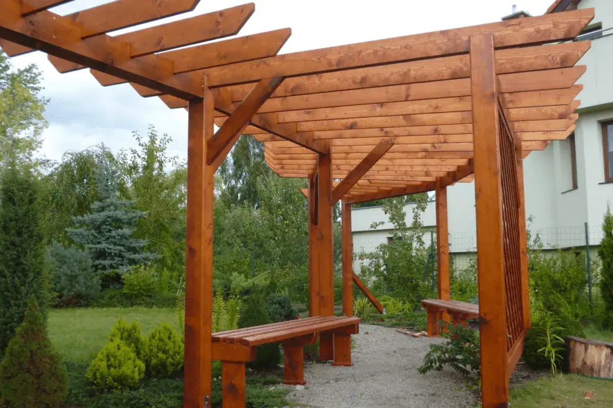 Drewniana pergola w ogrodzie, z ławkami, idealna do relaksu. Dowiedz się, jak zrobić pergole, by stworzyć własne zaciszne miejsce.