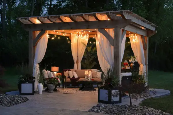 Urocza pergola z oświetleniem i zasłonami, idealna na letnie wieczory. Inspiracja, jak zrobić pergole, by stworzyć przytulne miejsce.