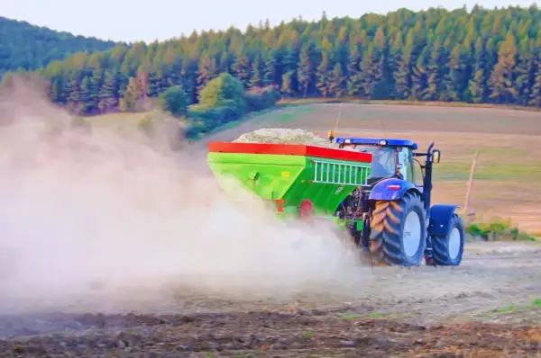 Traktor rozsiewa wapno, pomagając odkwasić glebę. W tle las i pole.